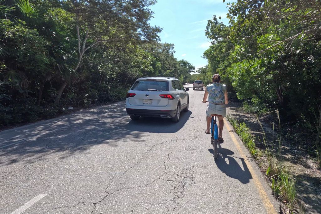 ride a bike next to a car on the road in Tulum