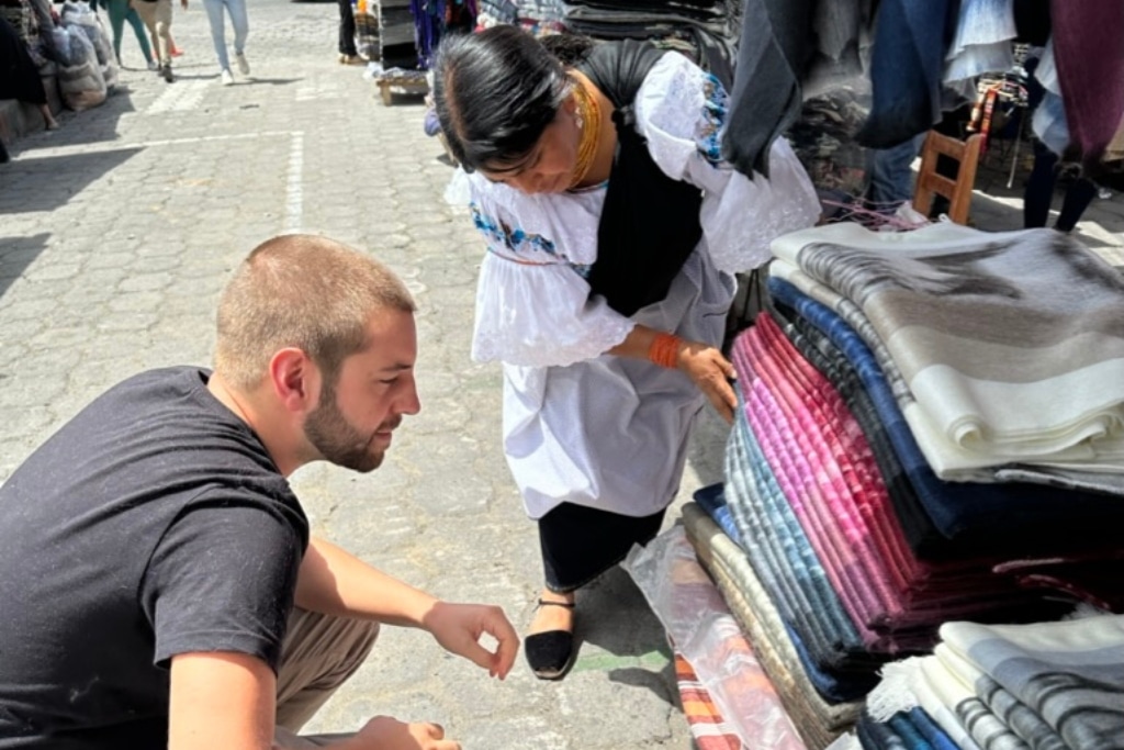 A man browsing a market stall in Otavalo with the help of an indigenous seller