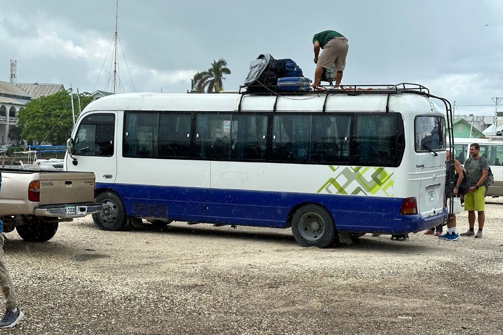 a man standing on the top of a mini bus tying the bags on the top