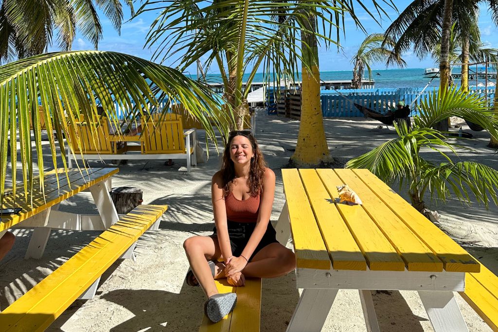 a girl sitting on a bright yellow picnic bench by the beach in belize