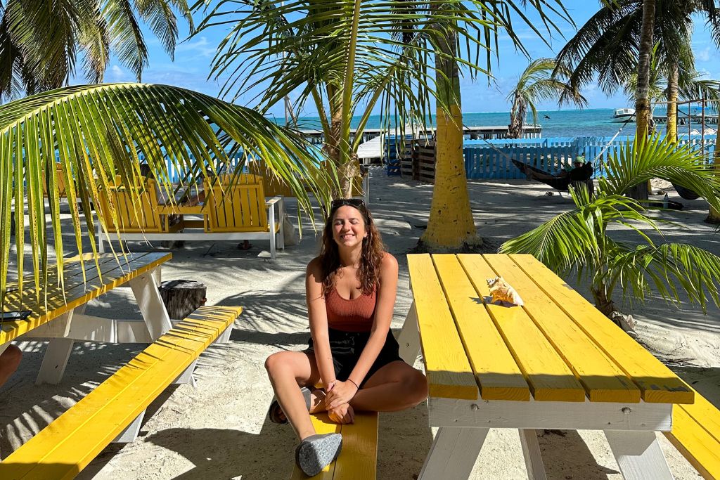 A gil sitting in the sun on a bright yellow picnic bench by the beach in Belize in December