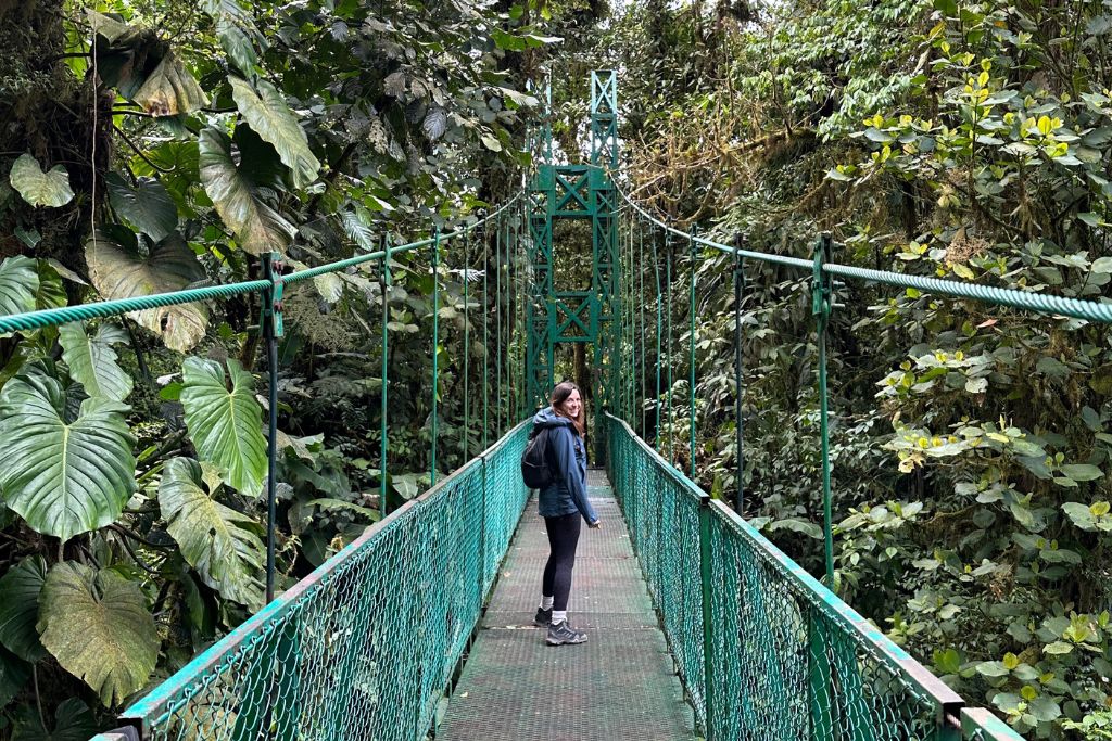 A girl walking across a green hanging bridge in Monteverde cloud forest surrounded by trees