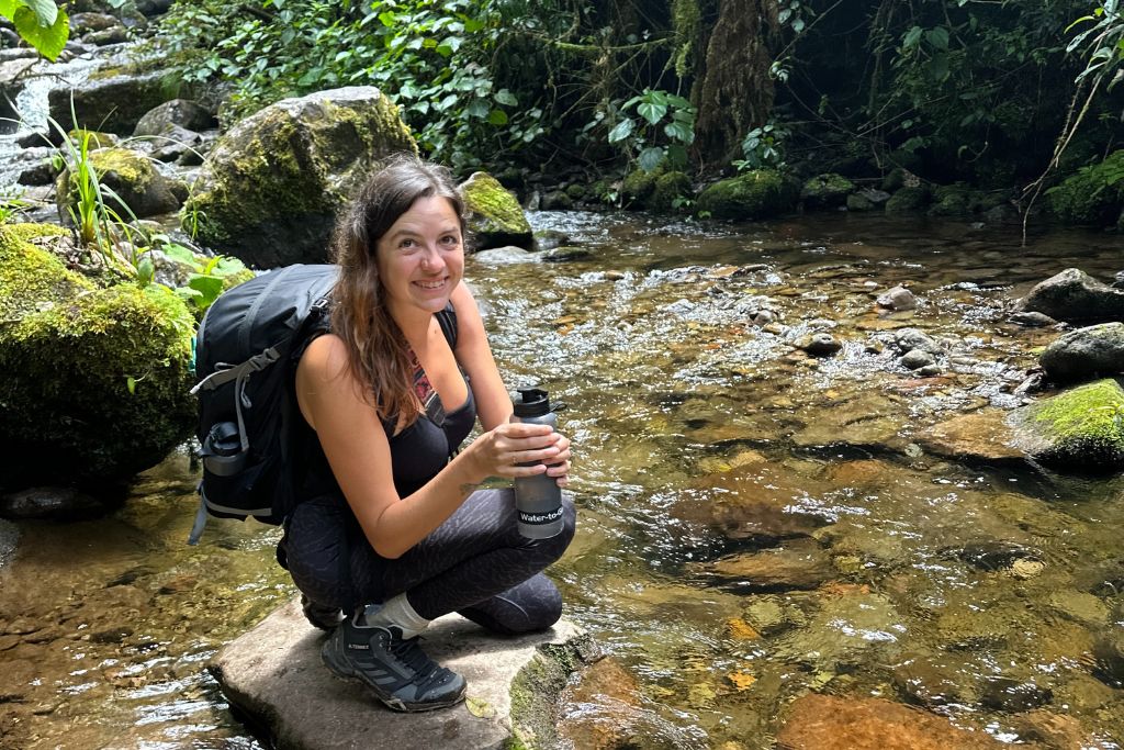 a girl filling a water bottle from a stream