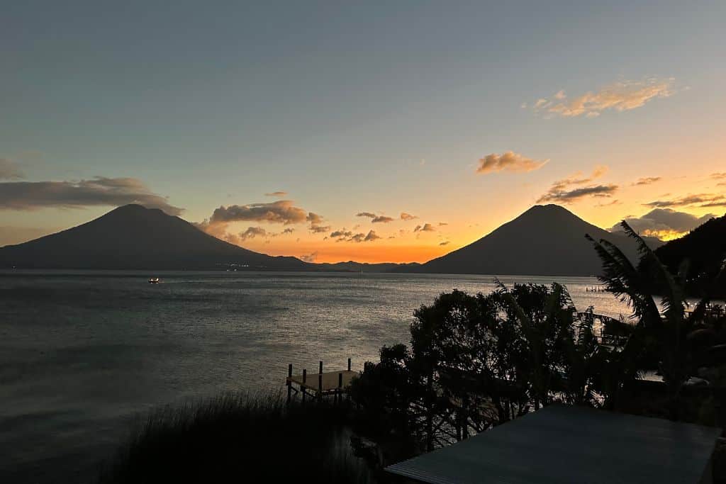 a view of the sun setting over lake atitlan with the volcanos in the distance