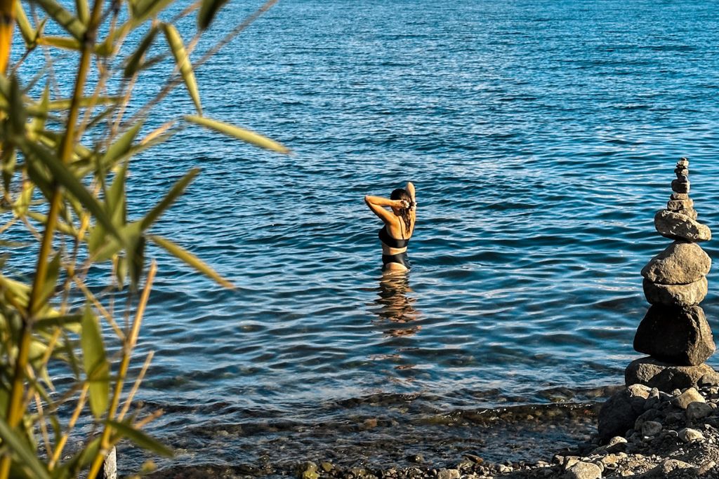 a girl standing in the water at lake atitlan with a stone tower on the shore
