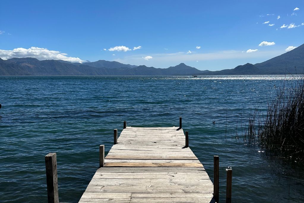 a long wooden pier over lake atitlan with a volcano in the distance