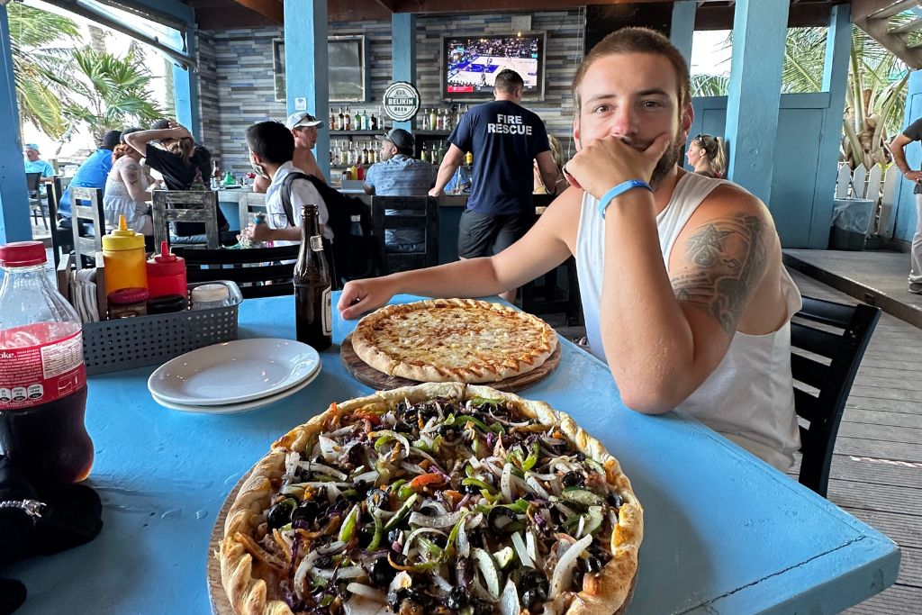 a man sitting at a restaurant tabel with 2 large pizzas in Belize